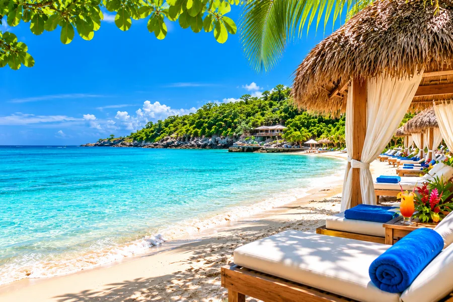 Turquoise Caribbean water and sandy beach with thatched cabanas at Blue Waters Beach Escape in Jamaica