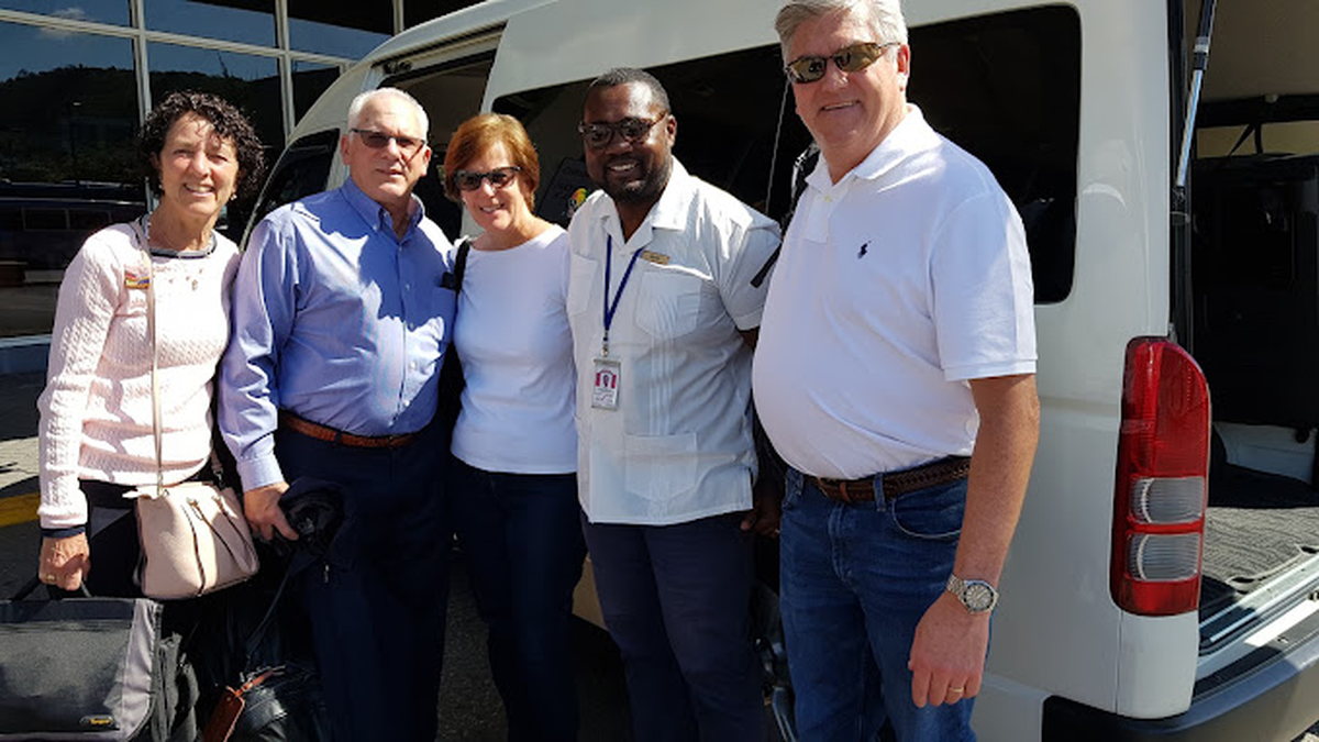 Happy tourists with their driver beside a private airport transfer vehicle in Jamaica